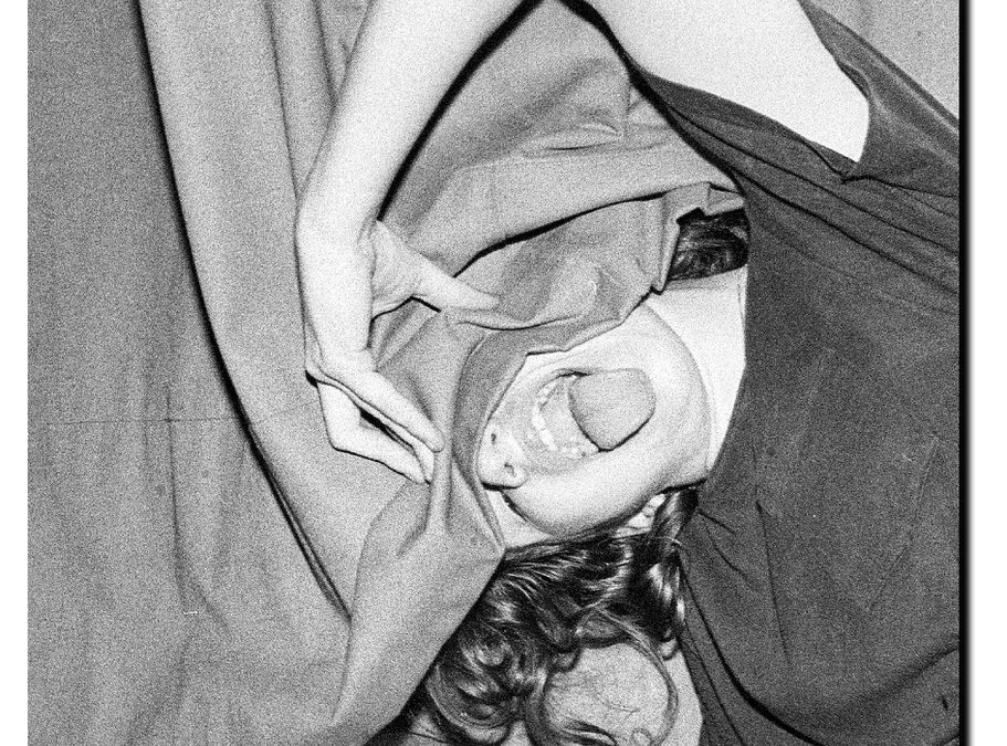Ein junges Mädchen aus den 80er Jahren. Sie streckt hinter einer Gardine dem Fotografen die Zunge heraus.